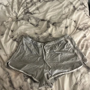 Grå shorts med snörning - Säljer ett par grå shorts med vit snörning i midjan. De har en avslappnad passform och är perfekta för en bekväm stil. Shortsen har vita kantdetaljer som ger en sportig look.