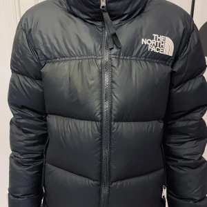 Svart dunjacka från The North Face - Säljer en snygg och varm svart dunjacka från The North Face. Jackan har en klassisk pufferstil med dragkedja framtill och är perfekt för kalla vinterdagar. Den är i nyskick och har långa ärmar för extra värme. ordinarie pris 3895, självklart äkta!