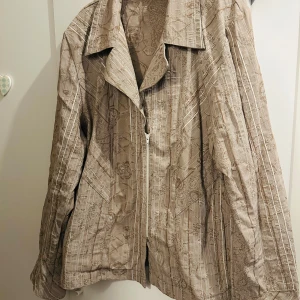 Beige mönstrad jacka med dragkedja - Säljer en beige kavaj med ett subtilt mönster och dragkedja framtill. Kavajen har en klassisk krage och långa ärmar. Perfekt för något stilrent men ändå unikt.