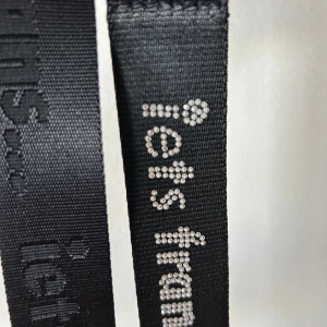 Svart bälte från Iets Frans - Säljer två svart bälte från Iets Frans. Det är gjort av ett slitstarkt material och har en cool, modern stil med märkets namn tryckt längs hela bältet. Perfekt för att ge en extra touch till din outfit!