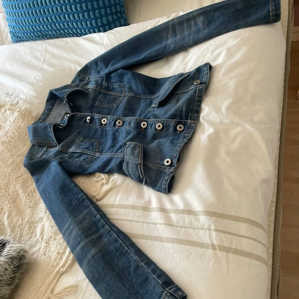 Säljer en snygg jeansjacka från D&G i klassisk blå denim. Jackan har en figursydd passform. Mått midja som bild 5, är  33 cm. Mått från armhåla till handled är  49 cm. Mått över byst  38cm. Står ingen storlek så XS är min gissning. . Jackor.