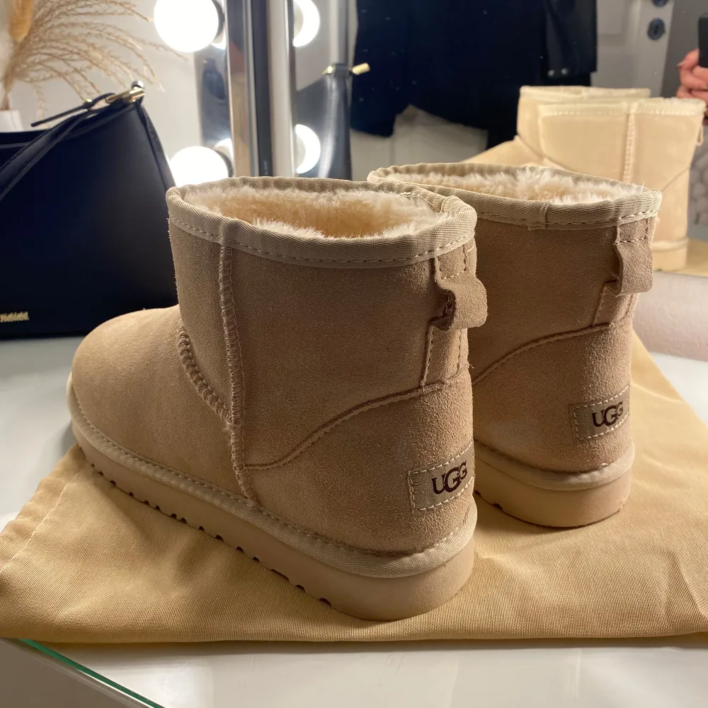 Supermysiga beige boots från UGG i mocka med fluffigt foder. Perfekta för kalla dagar när du vill hålla fötterna varma och bekväma. De har en klassisk design med rund tå och en robust sula för bra grepp. Passar perfekt till både vardag och avslappnade tillfällen. Äkta, helt nya aldrig använt, Tyvär var det ej min storlek! Lite ljusare än vad dem är på bild.❤️. Skor.