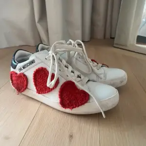 Superfina vita sneakers från Love Moschino med stora röda hjärtan på sidorna. De har snörning och är i bra skick. Skorna är i storlek 38, säljer då dessa inte kom till användning