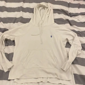 Vit Ralph Lauren hoodie - Säljer en stilren vit hoodie från Ralph Lauren med den klassiska loggan broderad i blått på bröstet. Den är i bra skicka förutom att den har en liten rosa fläck men ingen ser det ändå.           Hör av er vid frågor.