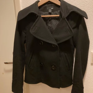 Svart kappa från H&M - Säljer en stilren svart kappa från H&M i mycket bra skick. Den har en klassisk dubbelknäppning med stora knappar och en snygg krage. Perfekt för höst och vår! Passar både till vardags och fest. 🖤