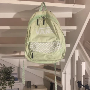 Grön ryggsäck från Vans - Säljer en snygg grön ryggsäck från Vans i mycket bra skick. Den har ett coolt rutigt mönster på fickan och justerbara axelremmar. Perfekt för skolan eller utflykter! Ryggsäcken har flera fack med dragkedja för enkel organisering. Passa på att köpa denna stiliga och praktiska väska! 💚