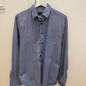 Mönstrad skjorta från East West - Säljer en snygg mönstrad skjorta från East West i storlek S. Skjortan är blå med ett diskret mönster och har långa ärmar. Perfekt för både vardag och fest! Den är i mycket bra skick och har knappar framtill.