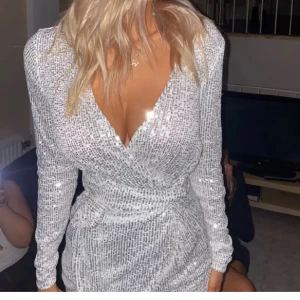 Glittrig silverklänning - Säljer en superfin glittrig silverklänning med omlott-design och långa ärmar. Perfekt för fest eller nyår! Klänningen har en tight passform som framhäver figuren och ger en glamorös look. Den är i mycket bra skick. ✨