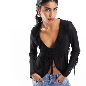 Svart blus med knytning - Snygg svart blus med djup v-ringning och knytning framtill. Den har långa ärmar och en elegant, figurnära passform. Perfekt för en kväll ute eller en stilfull vardagslook.