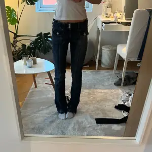 Säljer ett par mörkblå jeans i bra skick. De har en bootcut-stil och är dekorerade med knappar framtill. Lågmidjade. Har inga fickor på baksidan men på framsidan💞