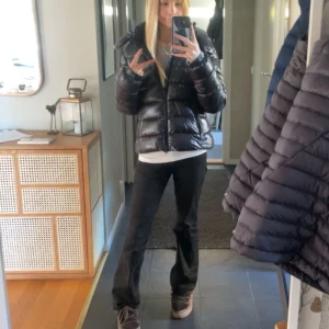 Svart pufferjacka  - Säljer en snygg svart pufferjacka i glansigt material. Jackan har en dragkedja framtill och en mysig huva. Perfekt för kalla vinterdagar. Helt ny, prislapp finns kvar och även kvitto.