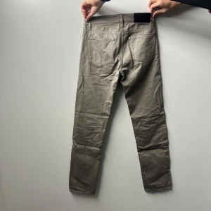 Grå byxor iggy ifrån Tiger of Sweden - Säljer ett par snygga grå byxor från Tiger of Sweden i modellen Iggy. De är aldrig använda och har en klassisk femficksdesign. 