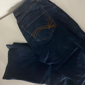 Mörkblå jeans med broderade bakfickor - Säljer ett par snygga mörkblå jeans med coola broderade detaljer på bakfickorna. De har en klassisk femficksdesign och ser ut att vara i bra skick. Perfekta för både vardag och fest! 🕺