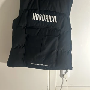 Svart dunväst från Hoodrich - Säljer en svart dunväst från Hoodrich i mycket bra skick. Västen har en stor ficka framtill och texten 'From Nothing to Something' tryckt längst ner. Perfekt för höst och vår, med en stilren design som passar till det mesta. Skön och varm för kyligare dagar.