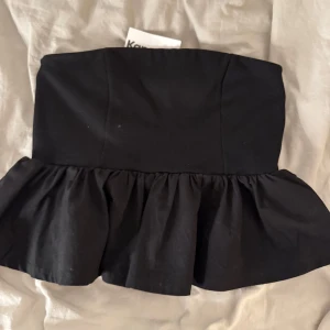 Svart tubtopp från Kappahl - Snygg svart tubtopp från Kappahl i storlek M. Toppen har en volangdetalj nedtill som ger en extra touch av stil. Perfekt för en utekväll eller fest. Helt ny med prislapp kvar!