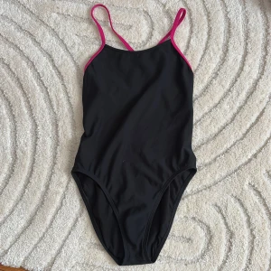 Svart baddräkt från Jolyn - Snygg svart baddräkt från Jolyn med rosa axelband och öppen rygg. Perfekt för simträning eller en dag på stranden. Tillverkad i 100% polyester för en bekväm passform och hållbarhet.  Nypris 800kr säljs för 180 kr. Pris kan diskuteras.