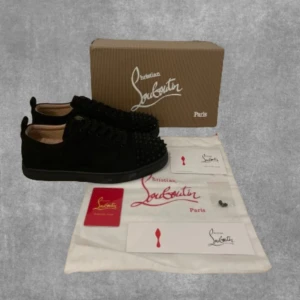 Svarta sneakers från Christian Louboutin - Snygga svarta sneakers från Christian Louboutin med ikoniska röda sulor och nitar på ovansidan. Skorna har snörning och är tillverkade i mocka, vilket ger en lyxig känsla🍾 Saknas en nit på ena skon men går att laga.