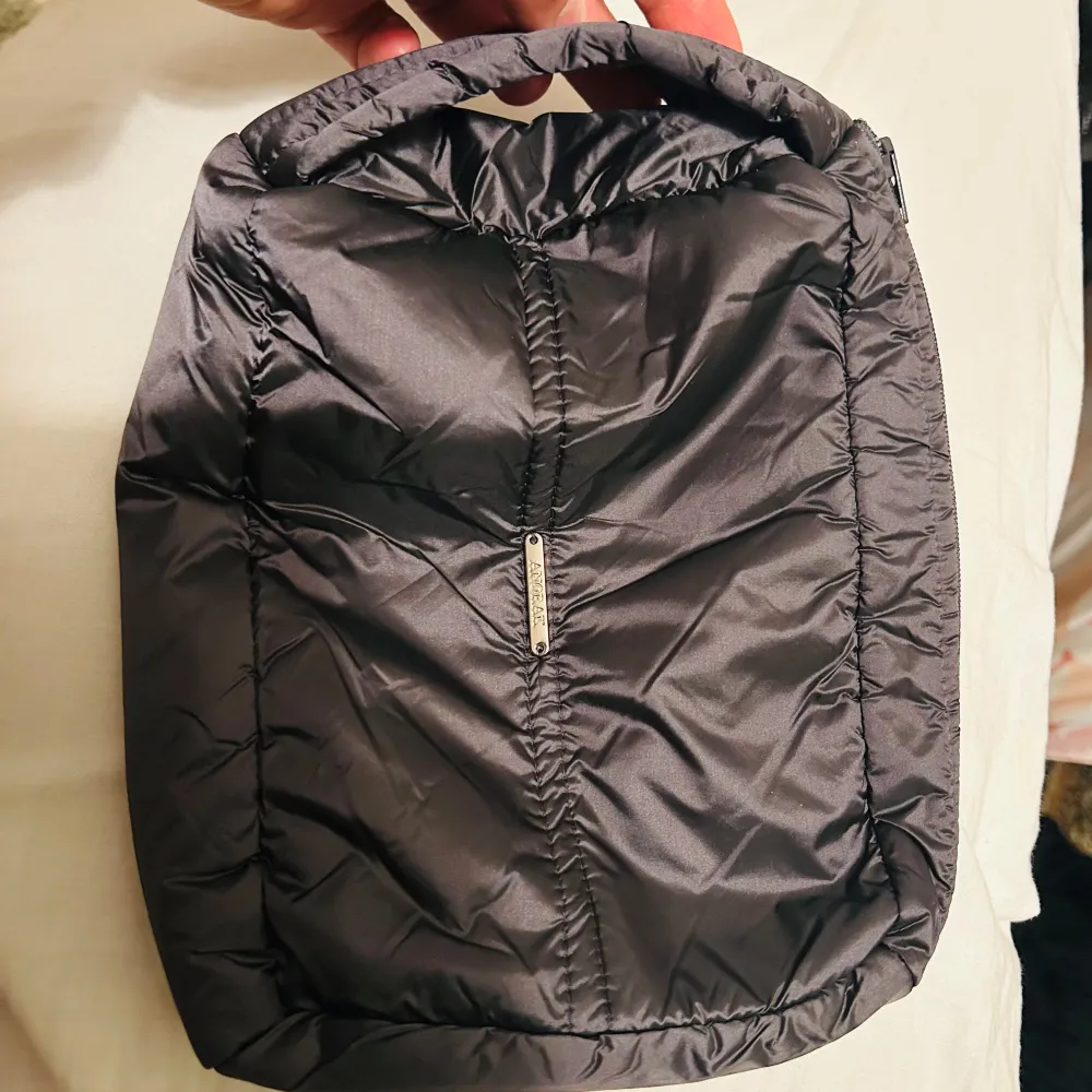 Snygg och praktisk mörkgrå sminkväska från Anorak. Tillverkad i syntetmaterial med en quiltad design och dragkedja för säker förvaring. Perfekt för att bära smink och smycken eller andra viktiga prylar.. Laukut & Käsilaukut.