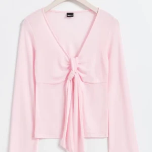 Rosa knytblus från Gina Tricot - Säljer en söt rosa blus/tröja från Gina Tricot med knytning framtill. Blusen har långa ärmar och en v-ringad design som ger en feminin touch. Perfekt för våren! Den har inte kommit till användning och det är storlek xs men passar s eftersom att jag brukar ha på mig s. ‼️Köpte den för 299kr‼️Jag står inte för frakt❤️