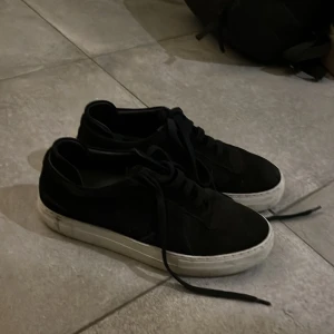 Svarta sneakers från Axel arigato - Snygga svarta sneakers med vit sula och snörning. Perfekta för en avslappnad stil. De har en klassisk design men ganska nötta då de är väldigt använda.        Skriv vid intresse