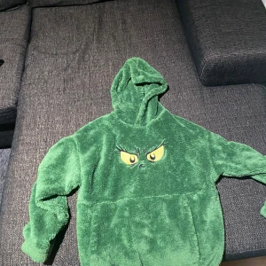 Grön fleece hoodie med tryck - Mysig grön fleece hoodie med ett tryck av ögon på framsidan. Perfekt för kalla dagar med sin fluffiga och varma känsla. Har en stor ficka framtill och en rymlig huva.