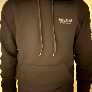 Svart hoodie från Moschino - Snygg svart hoodie från Moschino med logotyp på bröstet och längs ärmen. Är i väldigt bra skick använd några få gånger, köpt innan jul. Pris kan diskuteras.