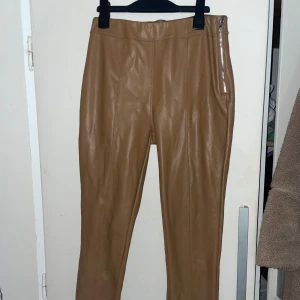 Beige skinnbyxor med dragkedja - Snygga beige skinnbyxor med en stilren dragkedja på sidan. Byxorna har en tight passform och är perfekta för en trendig look. De är högmidjade och ger en elegant siluett.