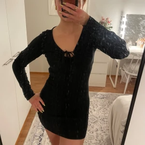 Svart klänning  - Snygg svart klänning från.  lång ärm och knytning framtill. Perfekt för en stilren look. 