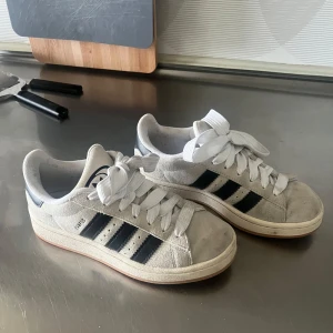 Vita Adidas sneakers med svarta ränder - Kan rengöra innan jag skickar iväg dem, använda max 10 gånger, nypris 1300 kr. Snygga Adidas Campus sneakers. Skorna har en vit sula och svart snörning. Perfekta för en avslappnad stil. Säljer ett par klassiska vita Adidas sneakers med svarta ränder och snörning. Skorna har en tidlös design med rund tå och är perfekta för en avslappnad stil.