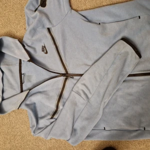 Ljusblå nike tech - Säljer en ljusblå hoodie från Nike med dragkedja och svarta detaljer. Jackan har en justerbar huva och långa ärmar. Perfekt för en sportig look eller en avslappnad dag. 🌀