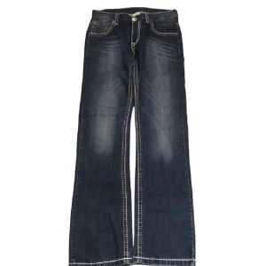 Mörkblå bootcut jeans från True Religion - Snygga mörkblå billy big T trueys med vit och orange stitch✨ Köpta på plick för några år sen men knappt använda av mig. Ena byxbenet har ett litet hål som syns på sista bilden!