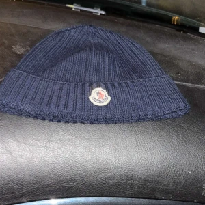 Mörkblå stickad mössa från Moncler - Snygg mörkblå stickad mössa från Moncler med ribbad kant och broderad logotyp framtill. Perfekt för kyliga dagar och ger en stilren look.