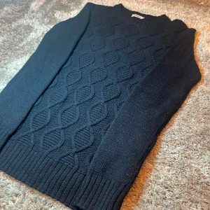 Kabelstickad J.Lindeberg tröja  - Snygg mörkblå stickad tröja från J.Lindeberg med en kabelstickad på framsidan. Tröjan har långa ärmar och ribbade muddar vid ärmslut och nederkant. 3% Kashmir i tröjan! Perfekt både i vardag och fest! Hör av dig vid minsta fråga!🤩