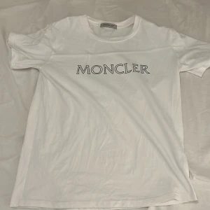 Vit t-shirt från Moncler - Säljer en stilren vit t-shirt från Moncler med deras ikoniska logga tryckt på bröstet. T-shirten har en klassisk rund hals och korta ärmar. Perfekt för en avslappnad och trendig look. Priset inte hugget i sten så bara att höra av er  mvh Viggo