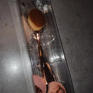 Sminkborste i roséguld - Snygg oval sminkborste med ett handtag i roséguld. Perfekt för att applicera foundation eller puder jämnt över ansiktet. Borsten är mjuk och tät, vilket ger en jämn och fin finish.