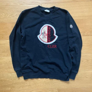 Svart Moncler Tröja - Snygg svart sweatshirt från Moncler med stort broderat logotypmärke på framsidan. Tröjan har långa ärmar och rund halsringning. Perfekt för en stilren och avslappnad look. Du vet varför den är så billig🐼🏴‍☠️. Den är i fint skick om man bortser från att märket på bröstet är lite nopprigt. Jag rekommenderar den starkt. Mitt pris är fast på 249kr förutom om man blir en följare då får man den för bara 199kr.