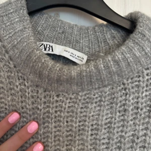 Grå stickad tröja från Zara - Säljer en mysig grå stickad tröja från Zara. Perfekt för kyliga dagar med sin varma och bekväma design. Tröjan har långa ärmar och en rund halsringning. Passar perfekt till både jeans och kjol. 