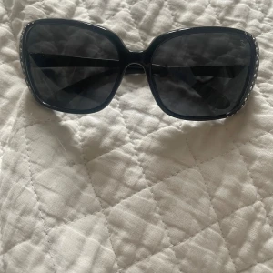 Svarta solglasögon med strassdetaljer från Bramdex - Snygga svarta solglasögon från Bramdex med stora bågar och glittriga strassdetaljer på sidorna. Perfekta för att ge en touch av y2k till din stil. De har en klassisk form som passar de flesta ansikten. De är mycket små, passar på småbarn.