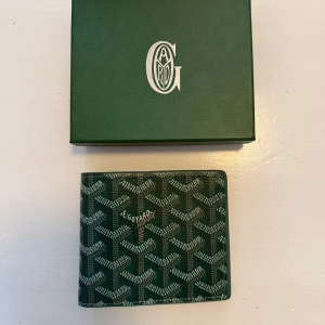 Grön plånbok  - Snygg grön plånbok från G*ya** med ett ikoniskt mönster. Plånboken har flera fack för kort och sedlar, perfekt för att hålla ordning på dina tillhörigheter. Den kommer i en matchande grön låda med logotyp.