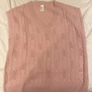 Rosa stickad väst - Säljer en söt rosa stickad väst med v-ringning och kabelstickat mönster. Perfekt för lager-på-lager stil och ger en mysig känsla. Passar bra till både skjorta och t-shirt.