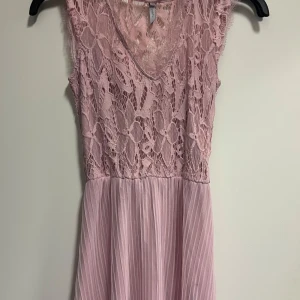 Rosa spetsklänning från HM - Säljer en superfin rosa långklänning från HM med spetsdetaljer och v-ringning. Klänningen har ett plisserat kjolparti och är ärmlös, perfekt för sommarens fester. 💖