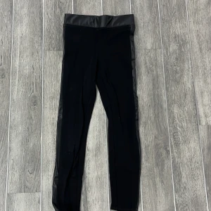 Svarta leggings från H&M - Snygga svarta leggings från H&M med hög midja och en glansig finish. Perfekta för en stilren look och kan enkelt matchas med olika toppar. De är tillverkade i ett stretchigt material som ger en bekväm passform.
