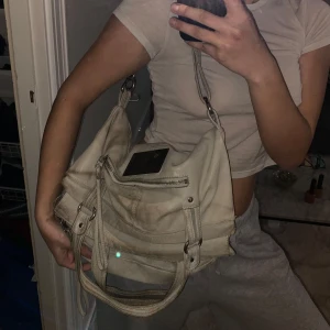 Zadig & Voltaire väska  - Säljer en snygg beige axelväska från Zadig & Voltaire. Väskan har en praktisk dragkedja och en cool metallplatta med logotyp. Perfekt för att bära med sig det nödvändigaste med stil. 