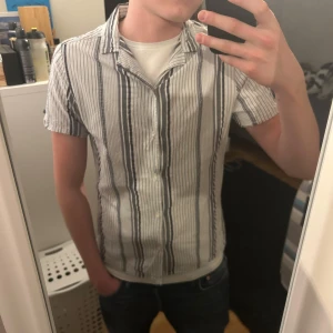 Randig kortärmad skjorta från Dressman  - Säljer en stilren randig skjorta från Dressman. Skjortan är kortärmad och har knappar framtill. Perfekt för en avslappnad look. Den är i en klassisk kombination av svart och vit. Hör gärna av er vid frågor:)