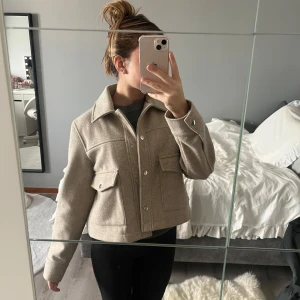 Beige jacka med knappar - Snygg beige jacka med knappar och två stora fickor framtill. Jackan har en klassisk krage och långa ärmar, perfekt för en stilren look. Passar bra till både jeans och kjol.