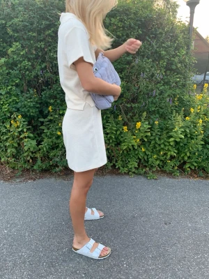 Quiltad axelväska med kedjerem - Säljer en quiltad axelväska i ljusblått tyg med tunna vita ränder. Väskan har en mjuk, puffig form och silverfärgade kedjeremmar som ger en cool kontrast. Perfekt storlek för det viktigaste och enkel att slänga över axeln.