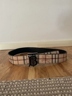 Beige rutigt Burberry bälte - Hej säljer nu mitt burberry bälte i ny skick, det har använts kanske 2 gånger men det helt nytt ut, inga skador eller liknande, du kan ändra loggan så bältet blir svart också vilken är en väldigt coolt funktion med detta bälte. Vid fler frågor så kom privat😁