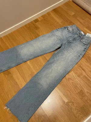 Ljusblå raka jeans från Zara - Säljer ett par ljusblå raka jeans från Zara med hög midja och råa, fransiga benslut. Jeansen har klassisk femficksdesign och är tillverkade i bomull. Perfekta för en avslappnad och trendig look.