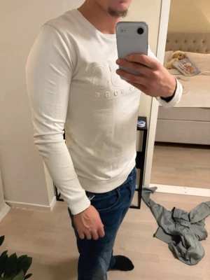 Vit långärmad tröja från Hugo Boss - Säljer en stilren vit långärmad tröja från Hugo Boss med diskret upphöjt logotryck på bröstet. Tröjan har rund halsringning och är tillverkad i mjukt material som sitter snyggt på kroppen. Perfekt för dig som gillar klassisk och enkel design. Pris kan diskuteras✅