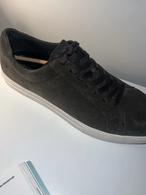 Mörkgrå mocka sneakers Vagabond - Helt nya stilrena mörkgrå sneakers i mocka med matchande mörka skosnören och vit sula. Aldrig använda. Klassisk låg modell som passar till det mesta och ger en clean look. Perfekta för dig som gillar minimalistisk stil och vill ha ett par snygga skor till vardags. 